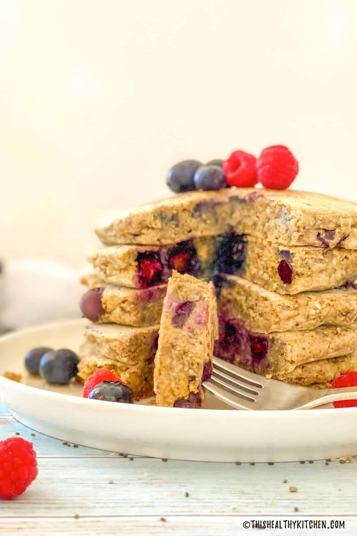 Stack of pancakes on plate with one bite on fork.
