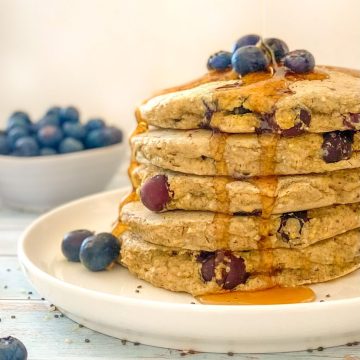 Syrup being poured over stack of blueberry pancakes.
