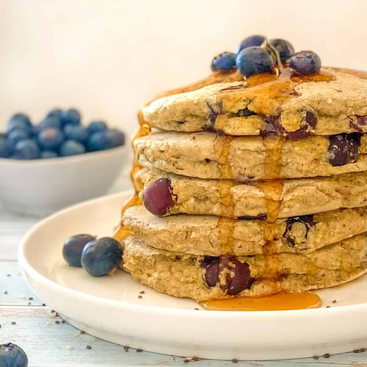 Syrup being poured over stack of blueberry pancakes.
