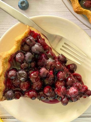 Slice of blueberry pie in white plate with fork.