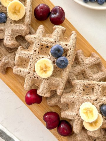 Waffles on cutting board with fresh fruit on top.