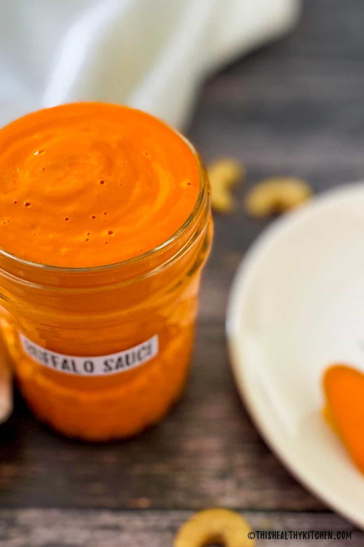 Jar of homemade vegan buffalo sauce with cashews around it.