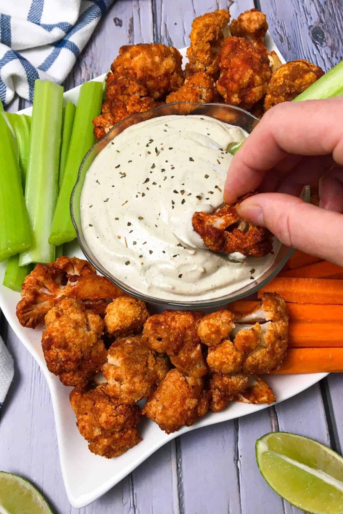 Hand dunking cauliflower wing into bowl of vegan ranch dip.