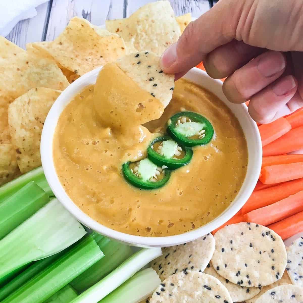 Hand dipping cracker into bowl of vegan cauliflower cheese sauce.