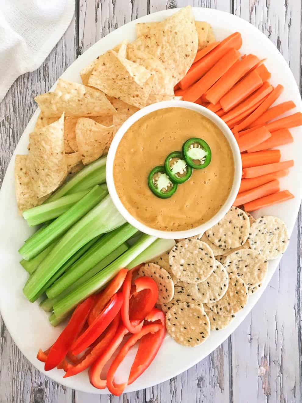 Platter with carrots, peppers, celery, chips and crackers and dip in the middle.