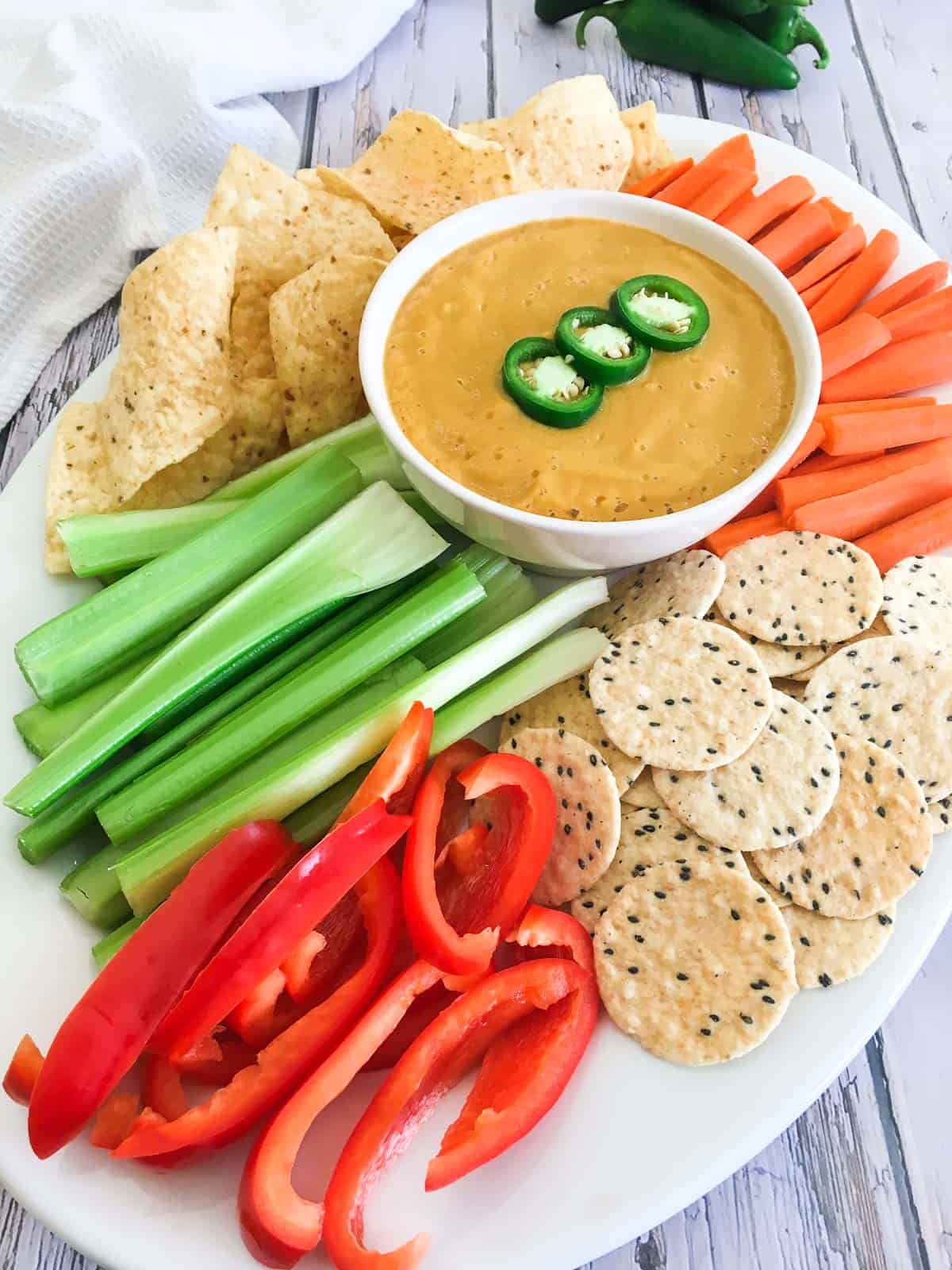Platter of chips, crackers and veggies with bowl of vegan cauliflower dip in the middle.