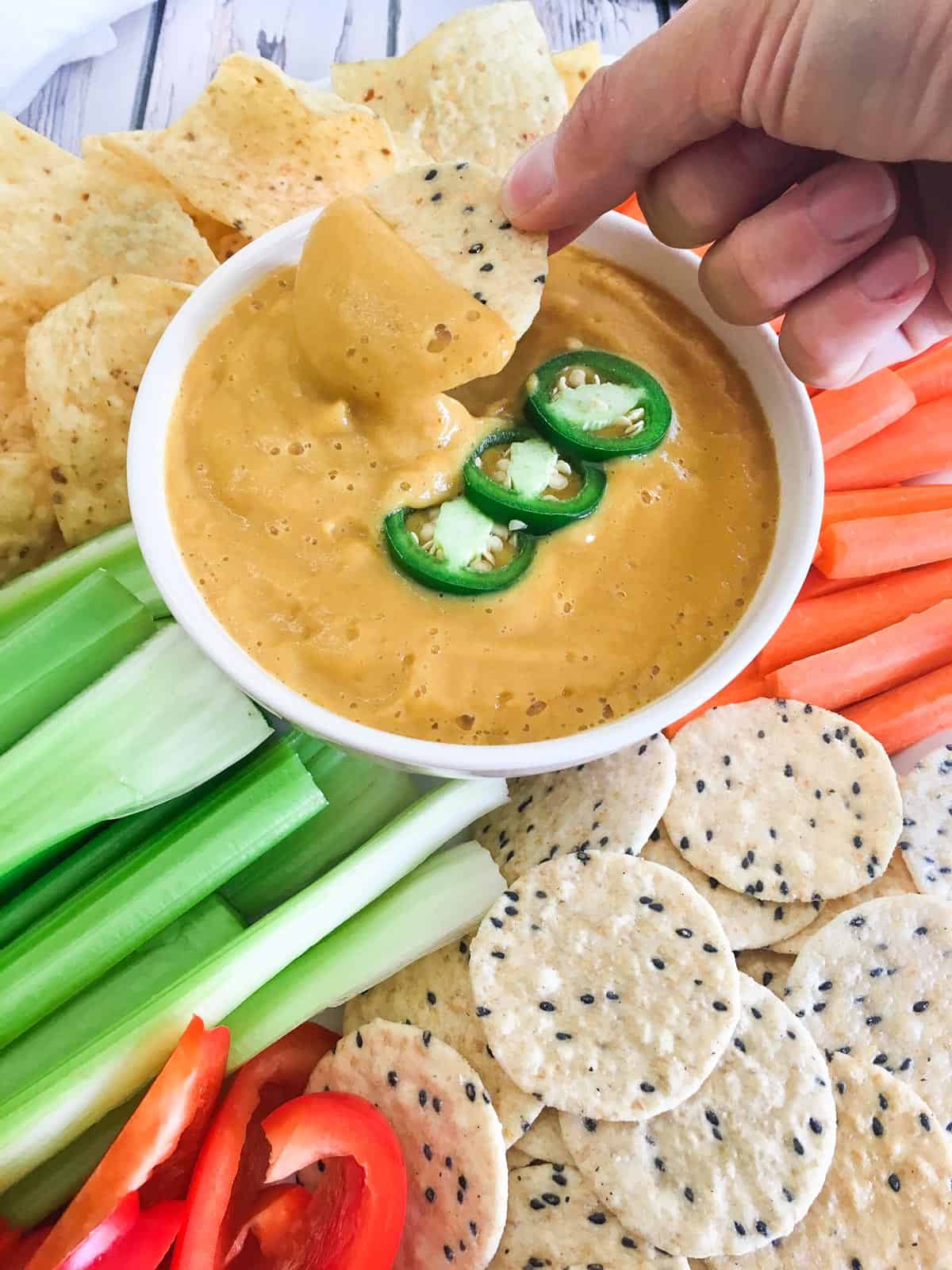 Hand dipping cracker into bowl of vegan cauliflower cheese sauce.