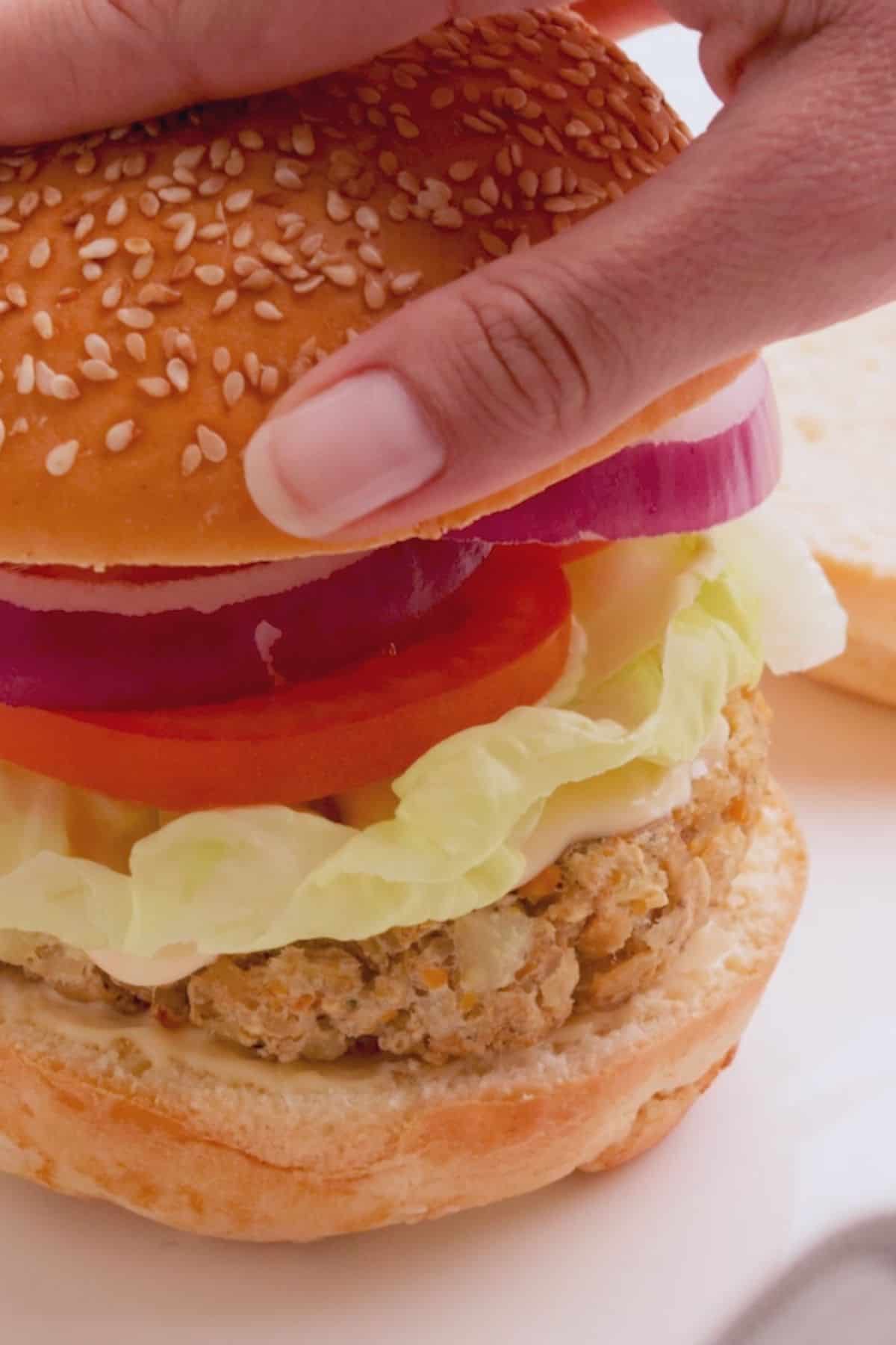 Hand placing top bun over burger and toppings.