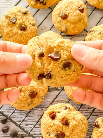 Hands breaking a chocolate chip cookie in half.