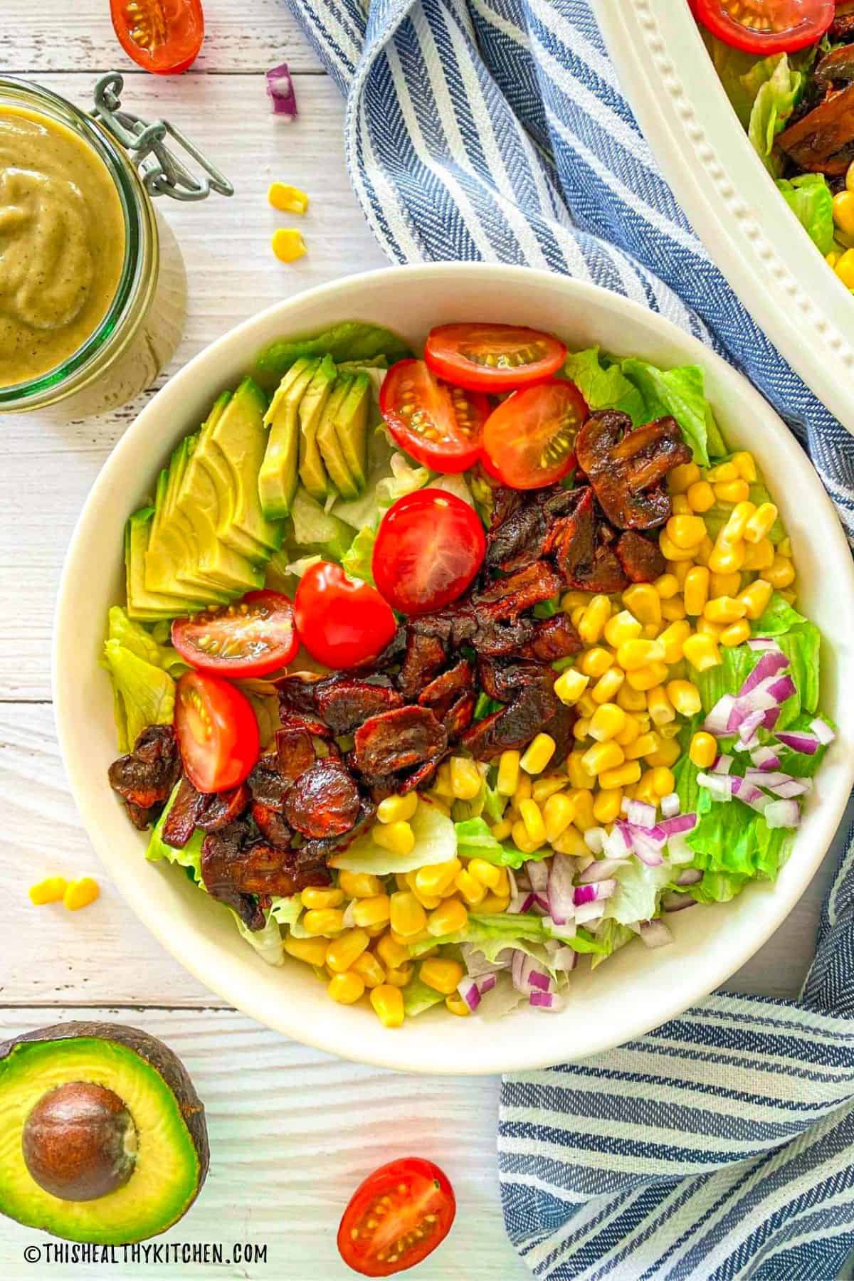 Vegan cobb salad with avocado, tomatoes, mushrooms, corn and onions.