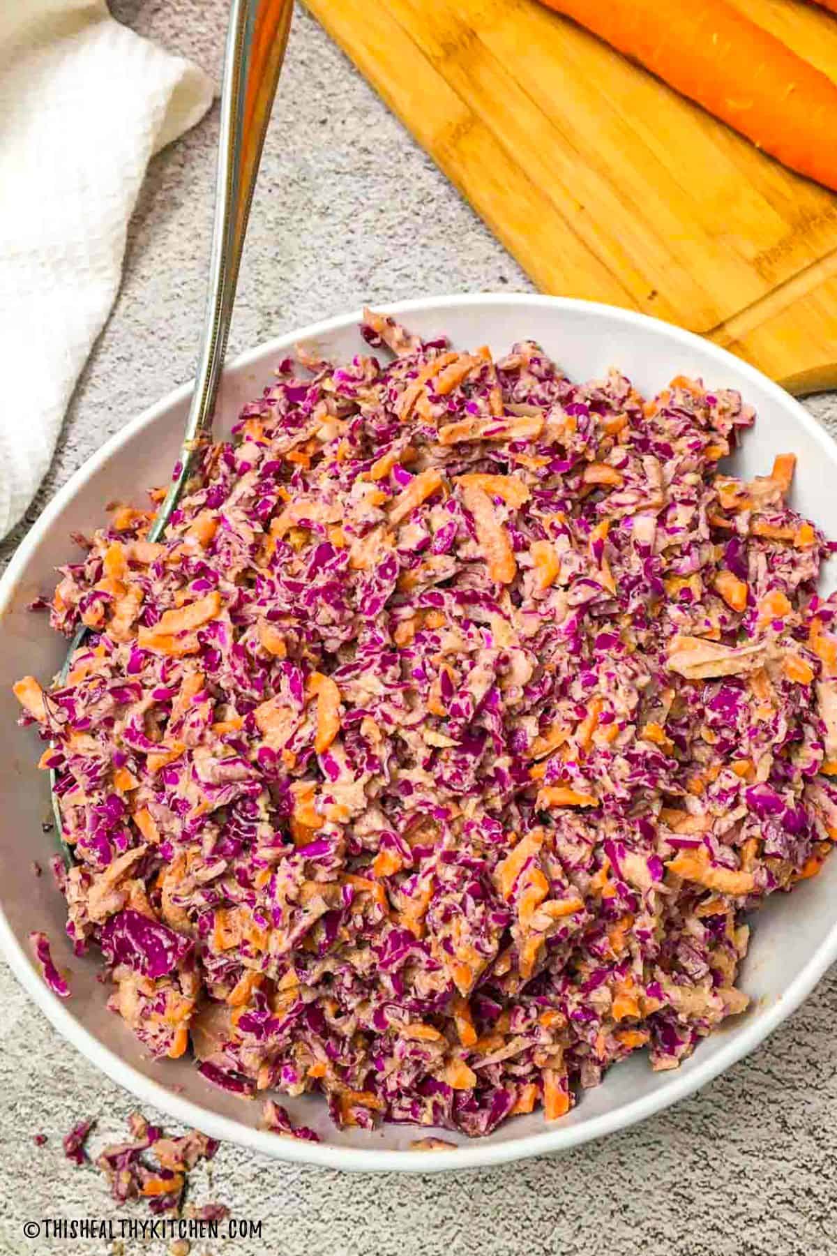 White bowl with coleslaw inside and carrot in the background.