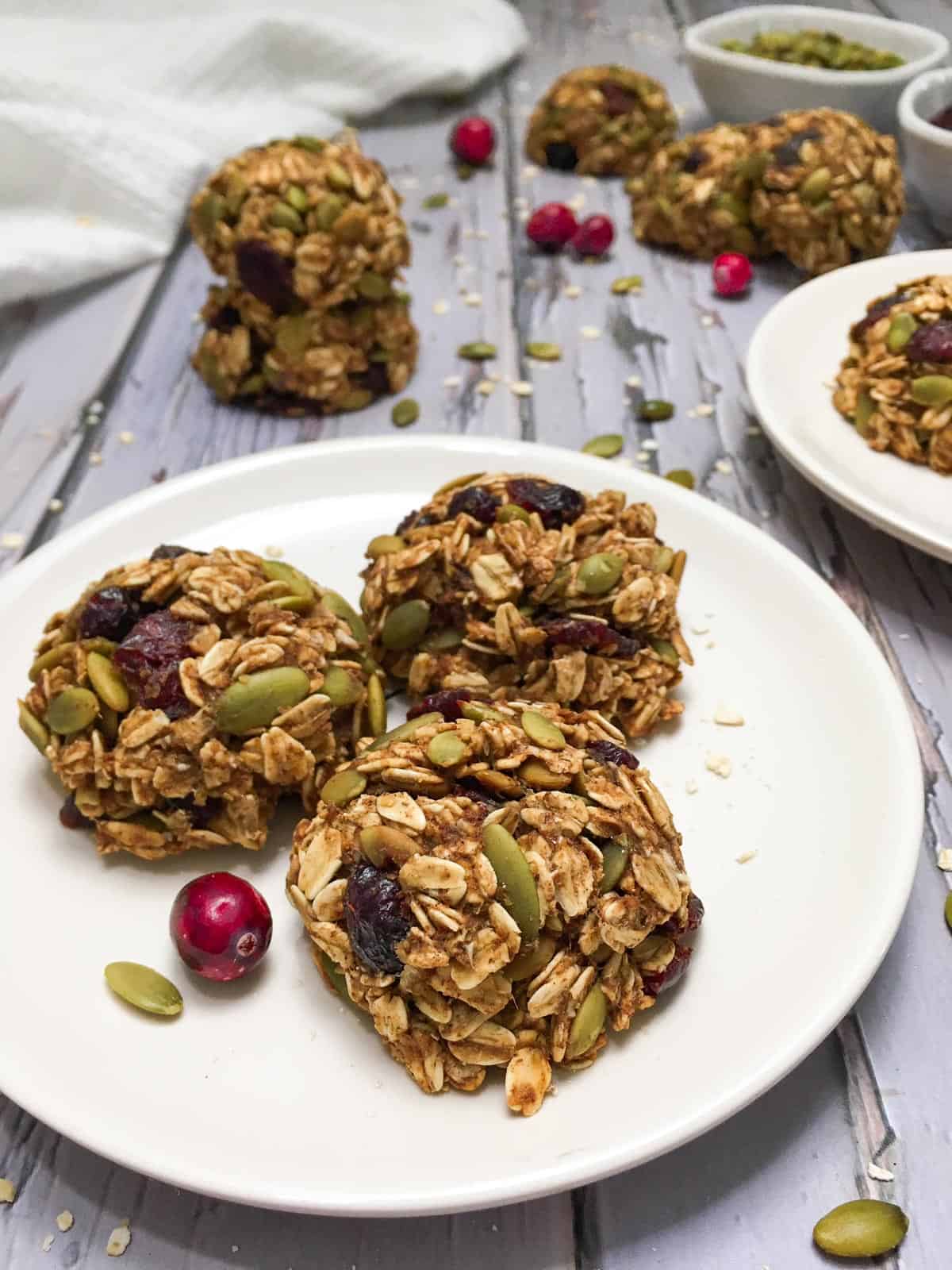 Three cranberry cookies on white plate with more cookies scattered in the background.