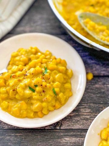 Vegan creamed corn in white plate with pan of more of it in background.