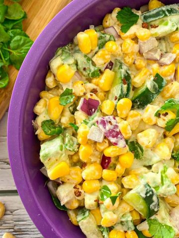 Bowl with corn salad and cutting board with cilantro, cucumber and lemon beside it.