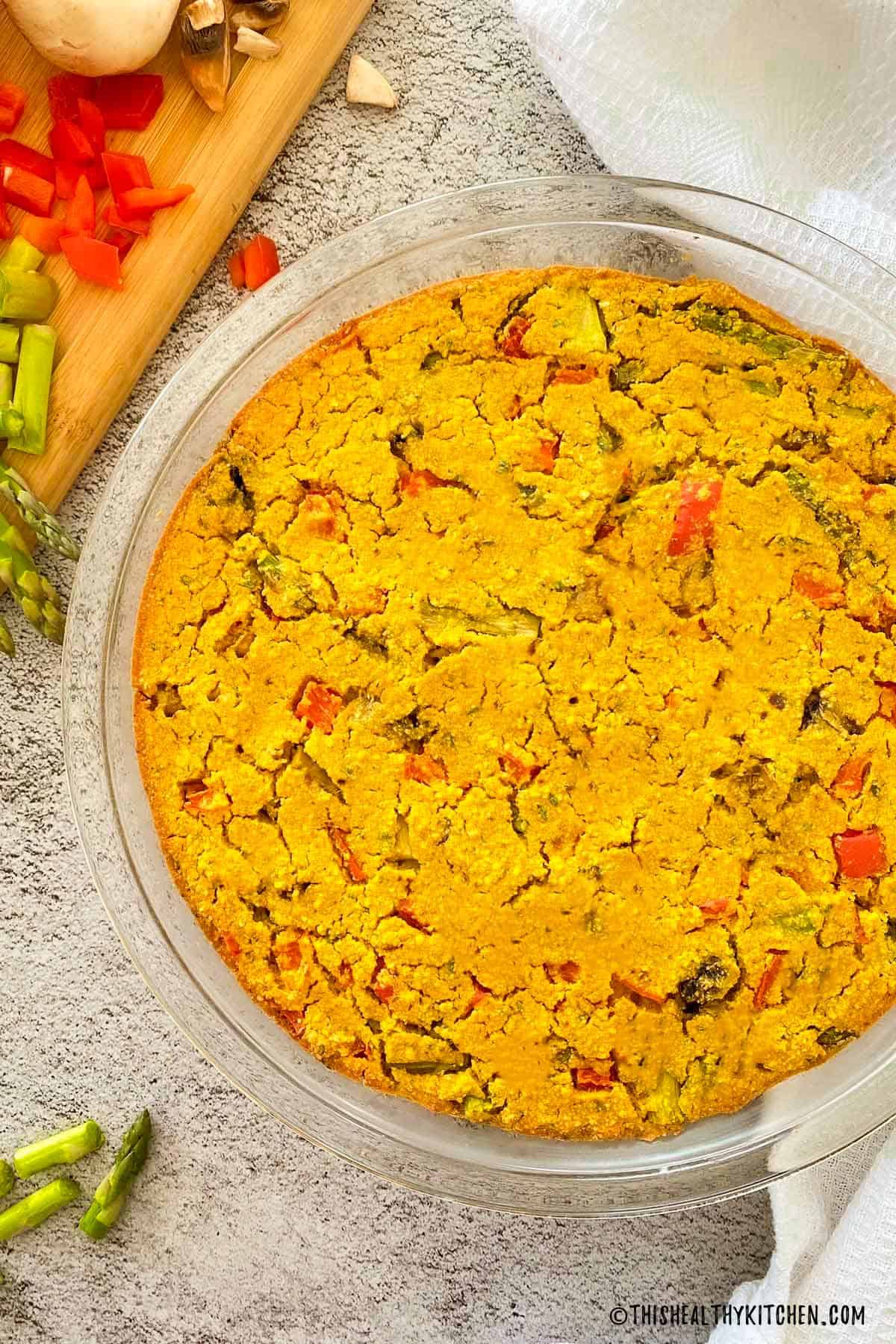 Vegan frittata in pie plate with asparagus and red peppers inside.