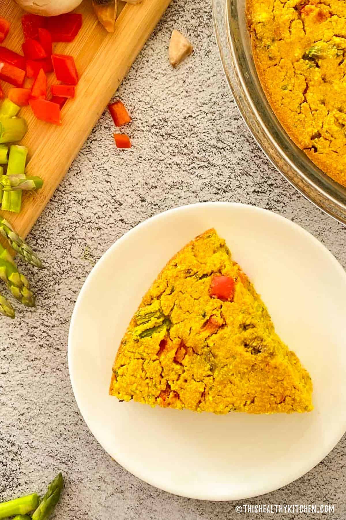 Slice of chickpea frittata in plate with remainder in pie plate behind.