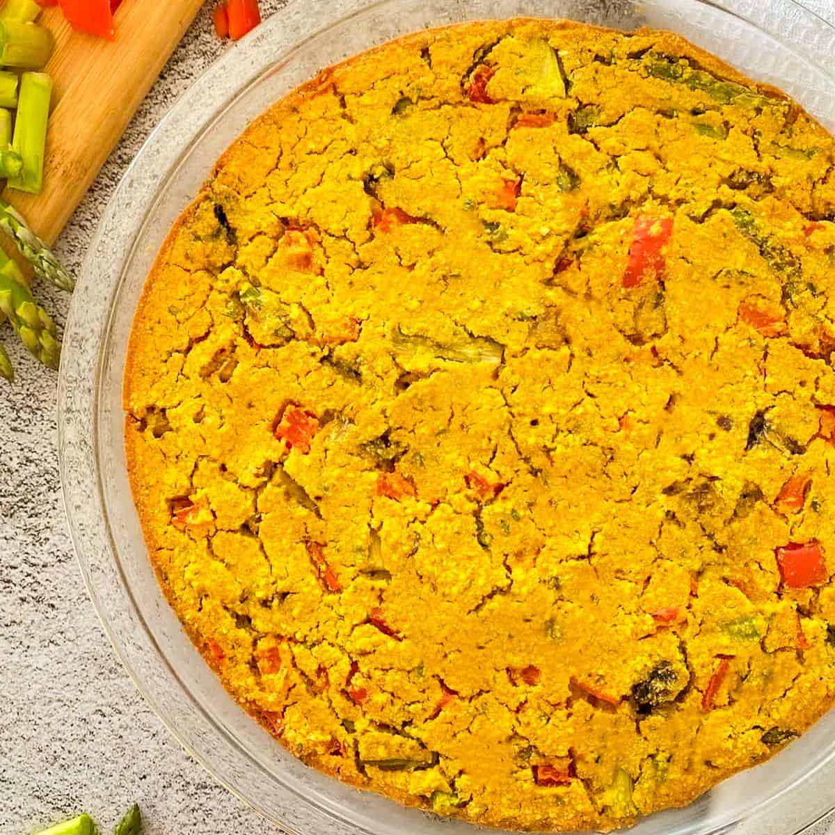 Vegan frittata in pie plate with asparagus and red peppers inside.
