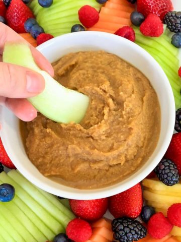 Slice of honeydew being dipped into bowl of dip.
