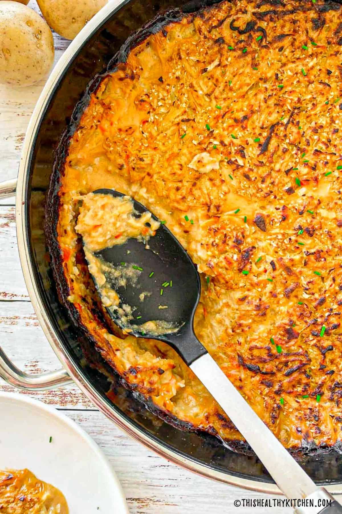 Vegan hash brown casserole in serving pan with serving spoon inside.