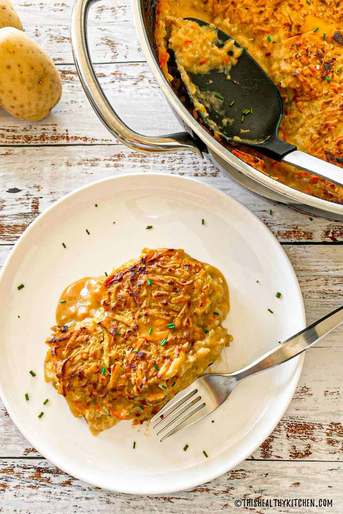 A slice of vegan hash brown casserole in white plate with remaining casserole beside it in pan.