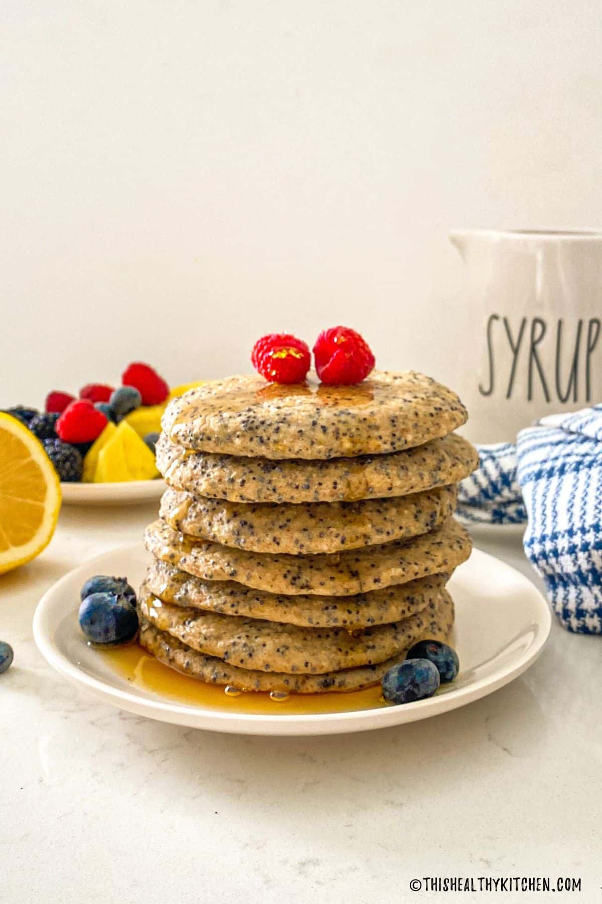 Stack of pancakes with raspberries on top and syrup dripping down the sides.