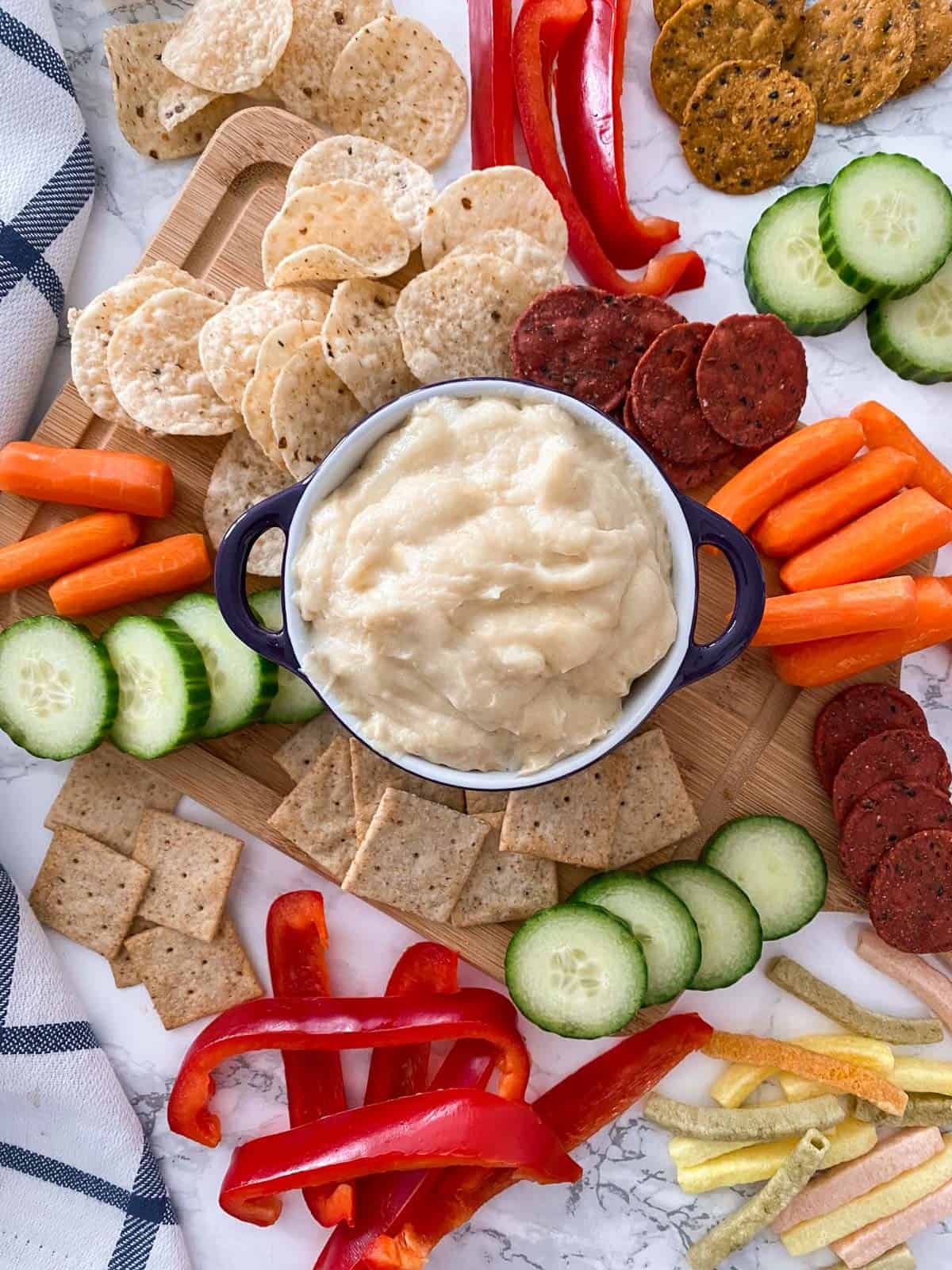 Bowl of cheese dip with chips, crackers and veggies scattered around it.