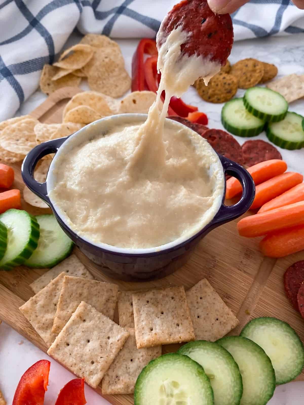 Cracker dipped in cheese dip being lifted from bowl.