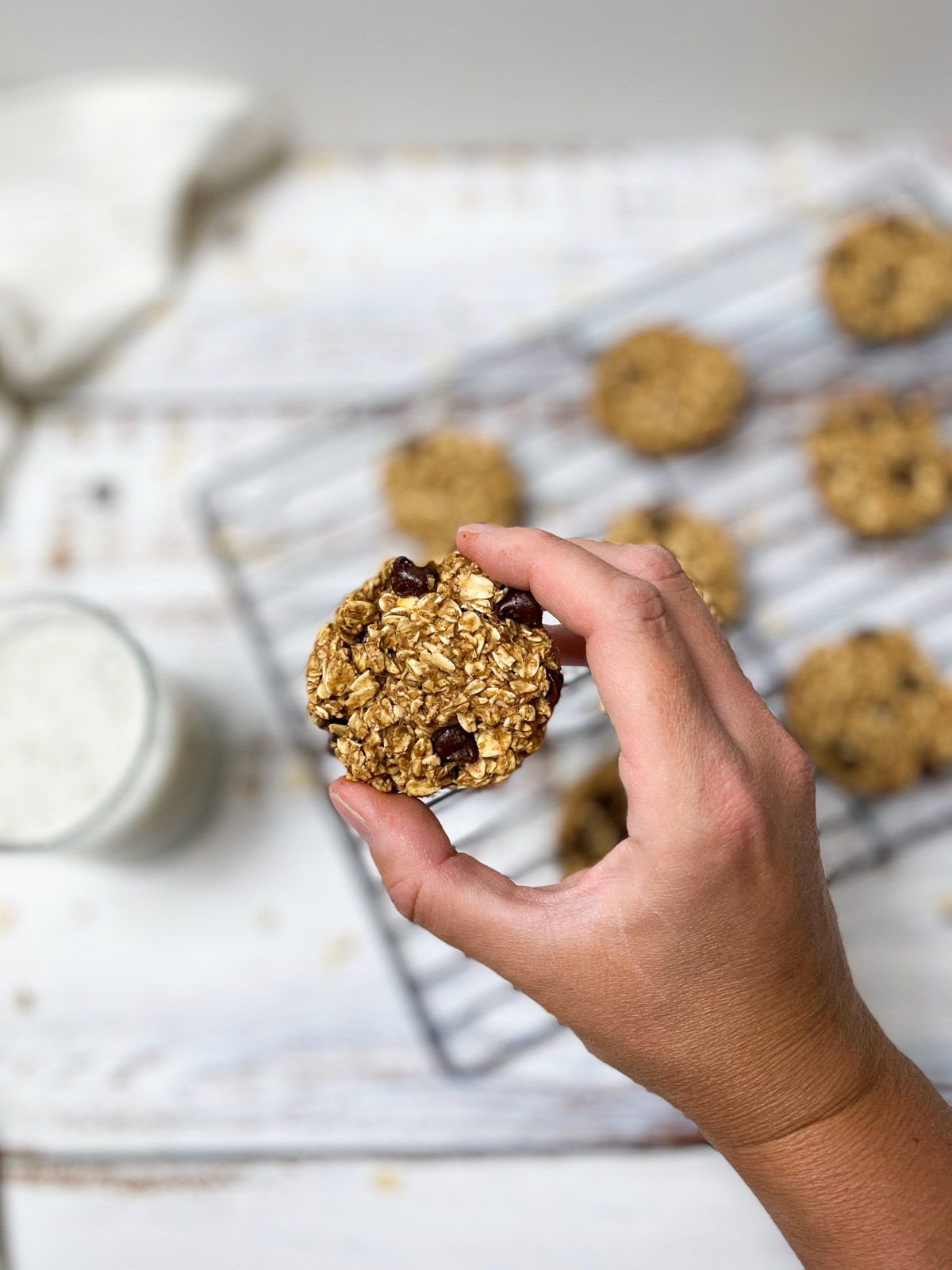 hand holding up a vegan oatmeal cookie above wire rack of cookies