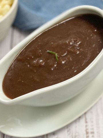Gravy boat filled with brown gravy and rosemary garnish.