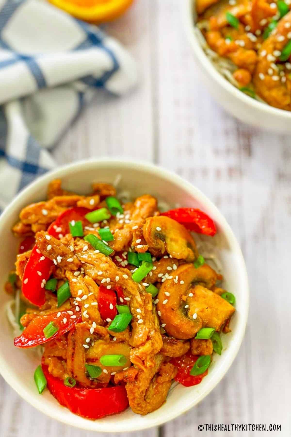 Vegan orange chicken with red peppers and mushrooms and sesame seeds on top.