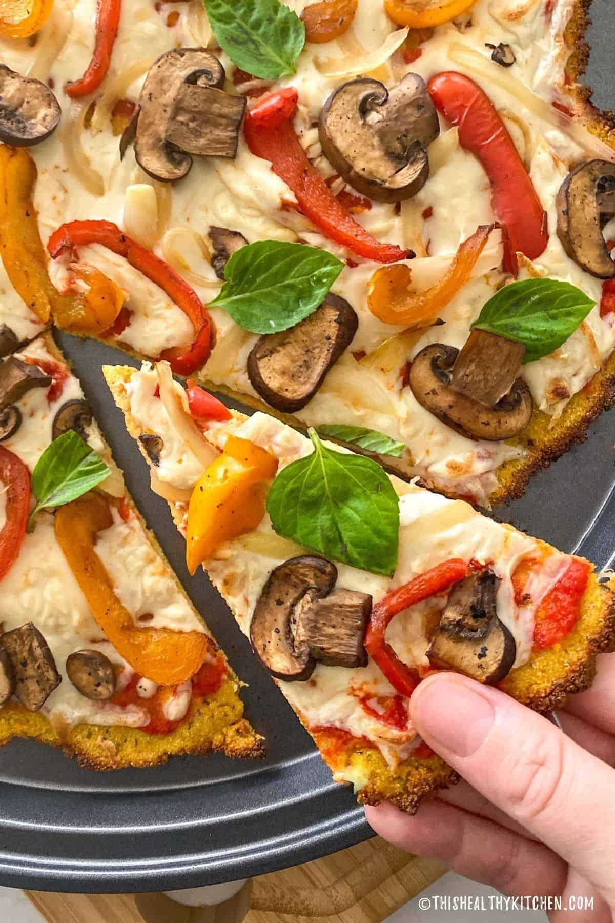 Hand grabbing slice of pizza from pizza tray.