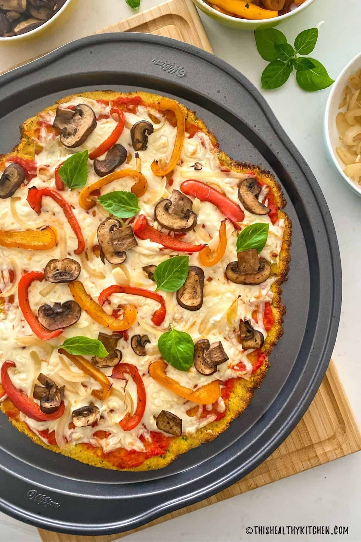 Polenta pizza with sauce, cheese and veggies on round pizza pan on cutting board.