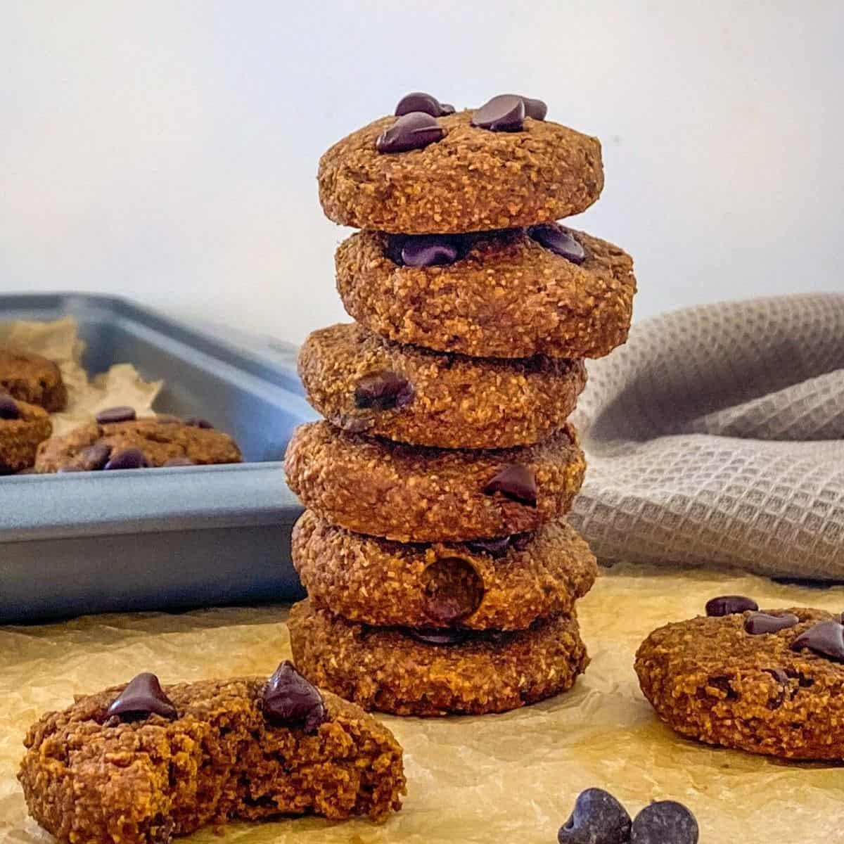 Stack of chocolate chip cookies with tray of more cookies in background.