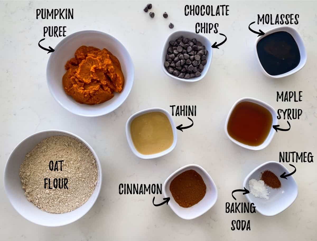 Ingredients required to make pumpkin chocolate chip cookies scattered in prep bowls on countertop.