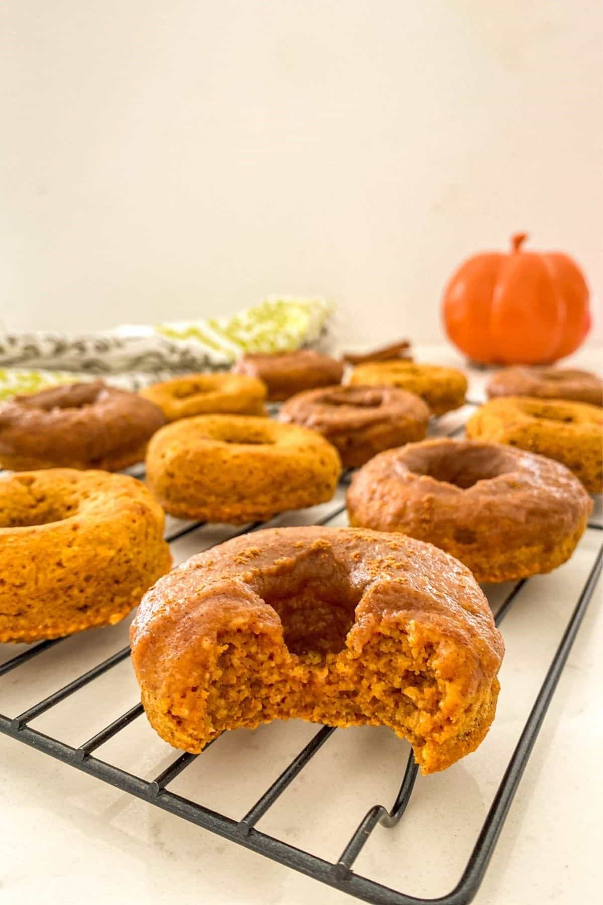 Angle view of donuts on cooling rack with bite taken out of first one.