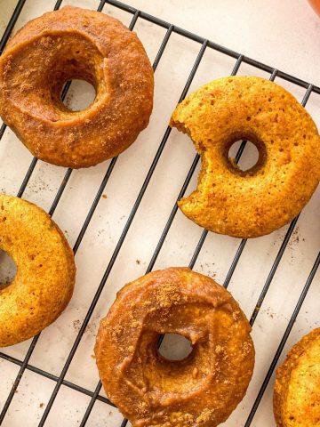 Pumpkin donuts on cooling rack with bite taken out of one of them.