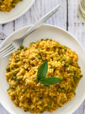 white plate with pumpkin risotto and fork on top and sage garnish.