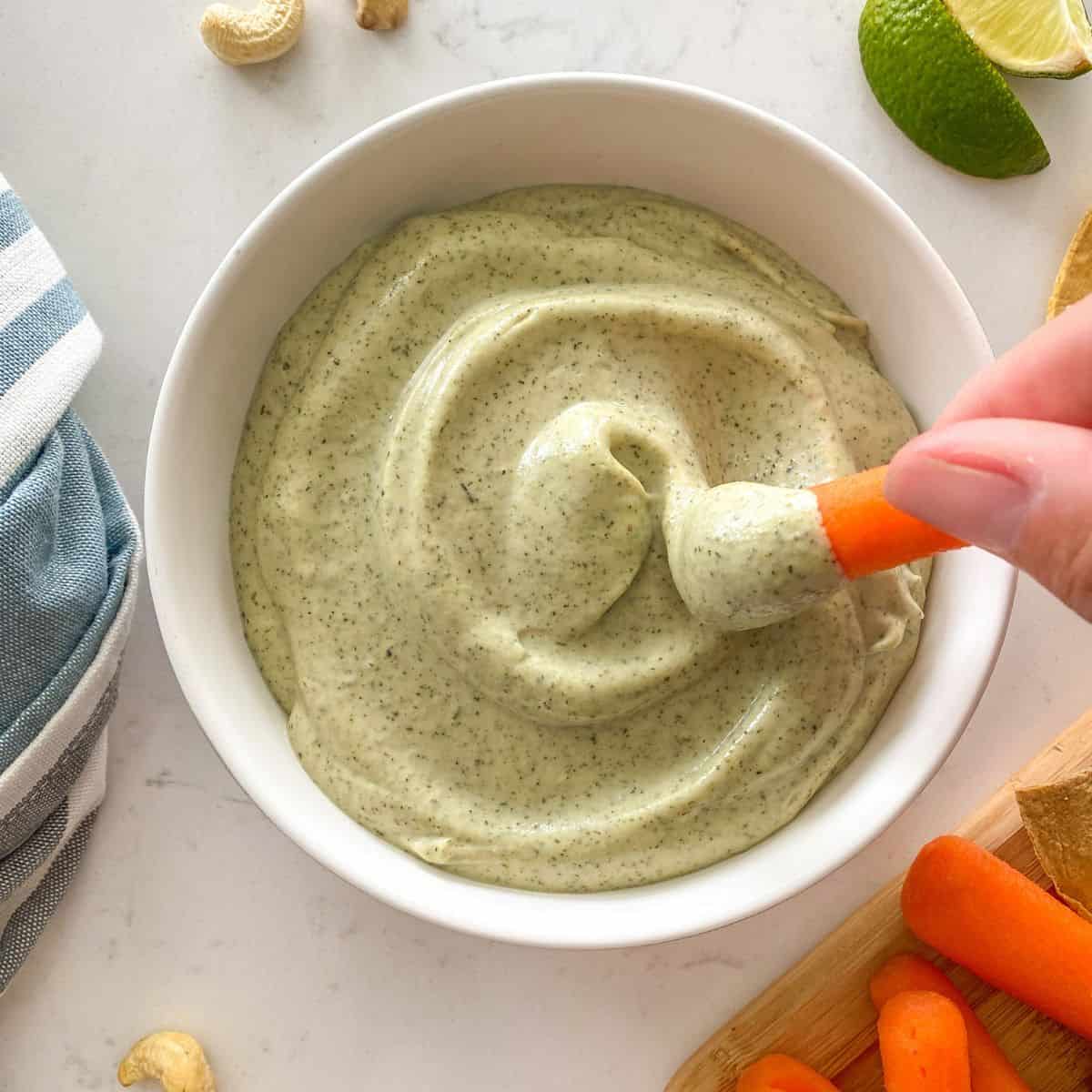 Vegan ranch dip in white bowl with carrot being dipped inside.