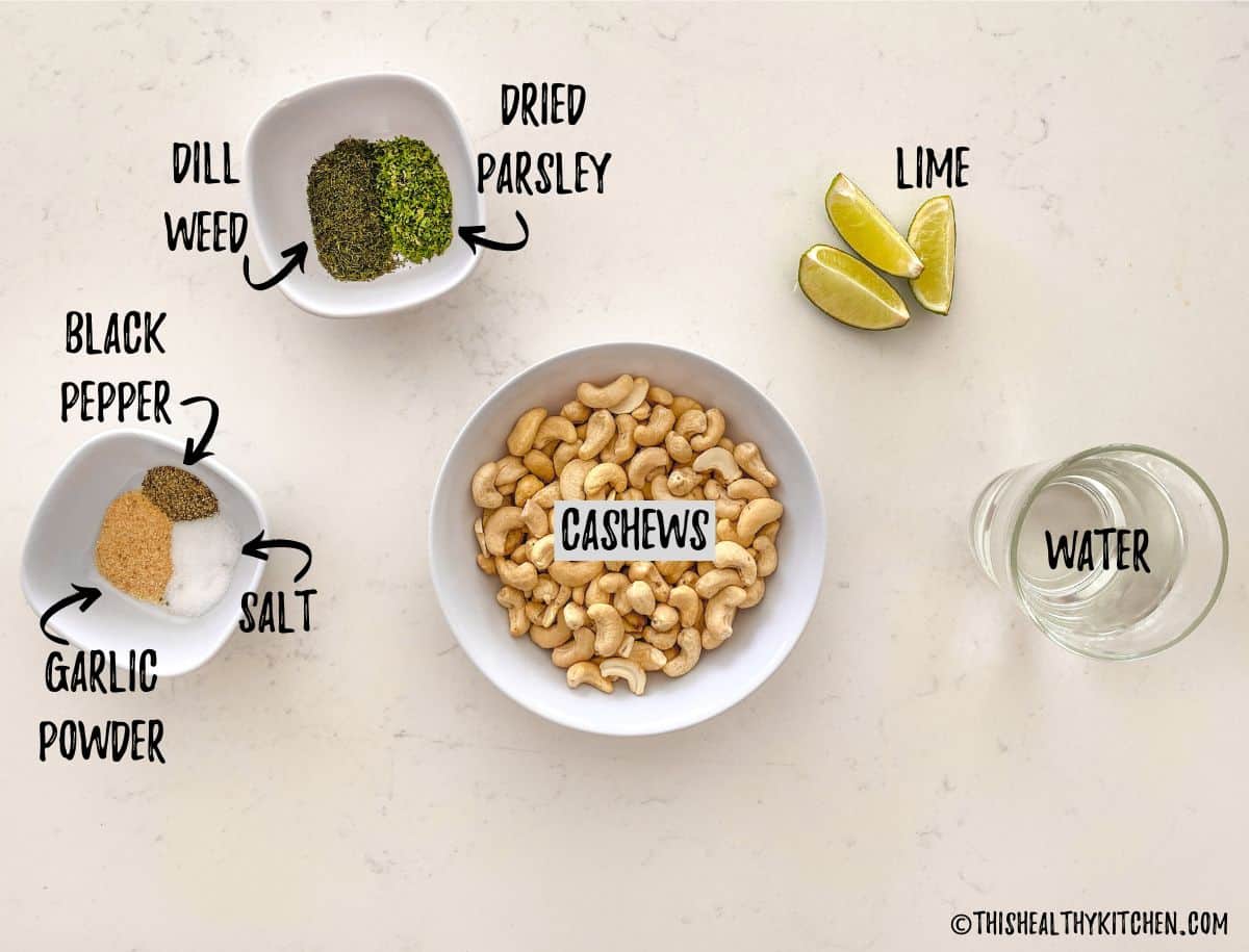 Bowls of spices, bowl of cashews, cup of water and lime wedges scattered on kitchen counter.
