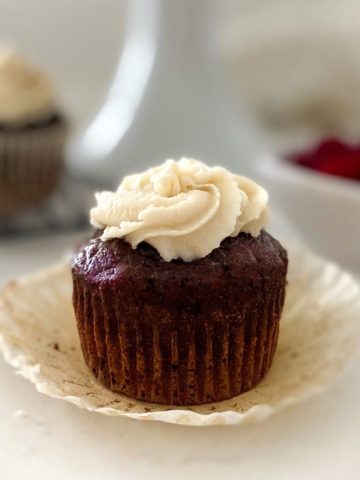 Red velvet cupcake sitting on cupcake liner with white frosting on top.