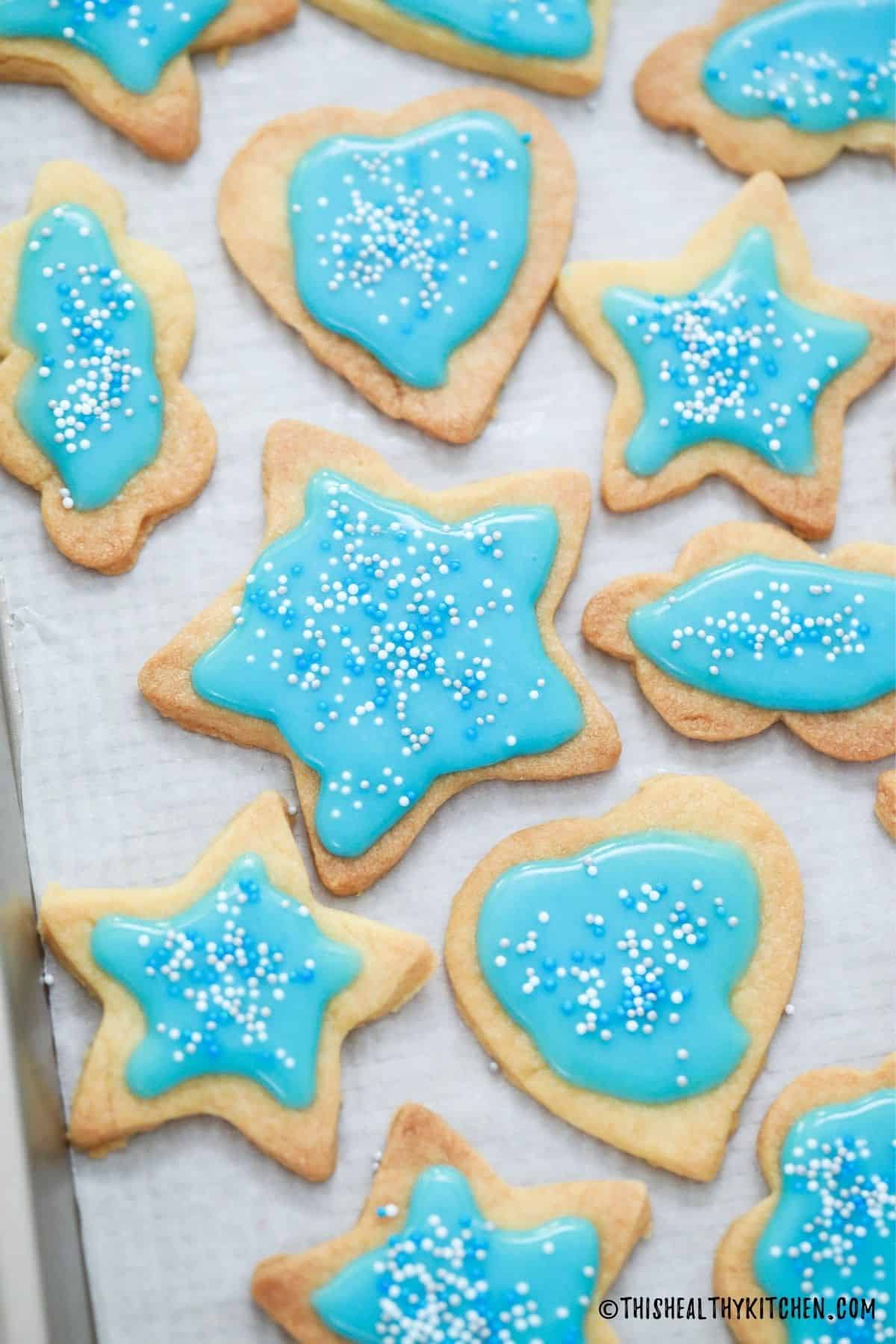 Shortbread cookies on baking sheet with blue icing and sprinkles on top.
