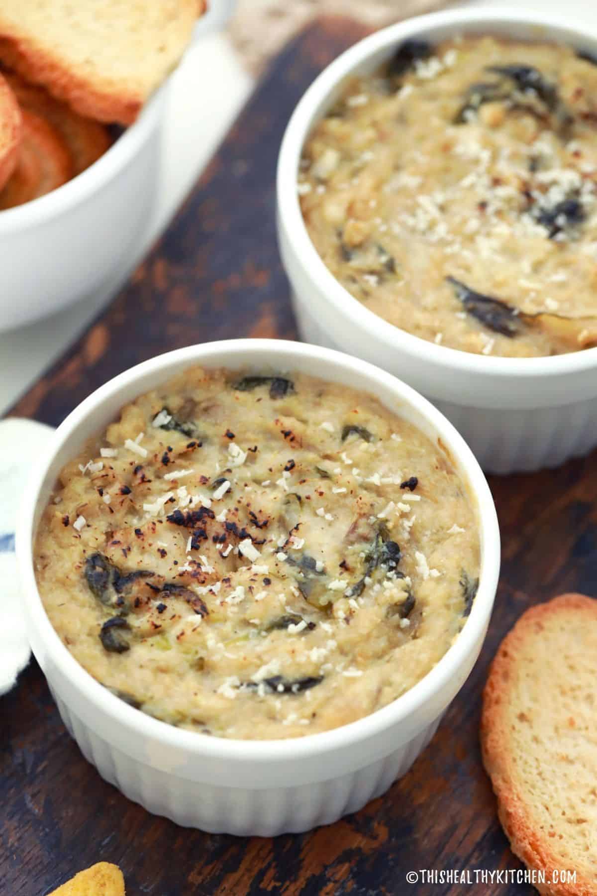 Two bowls of vegan spinach dip sitting on cutting board.