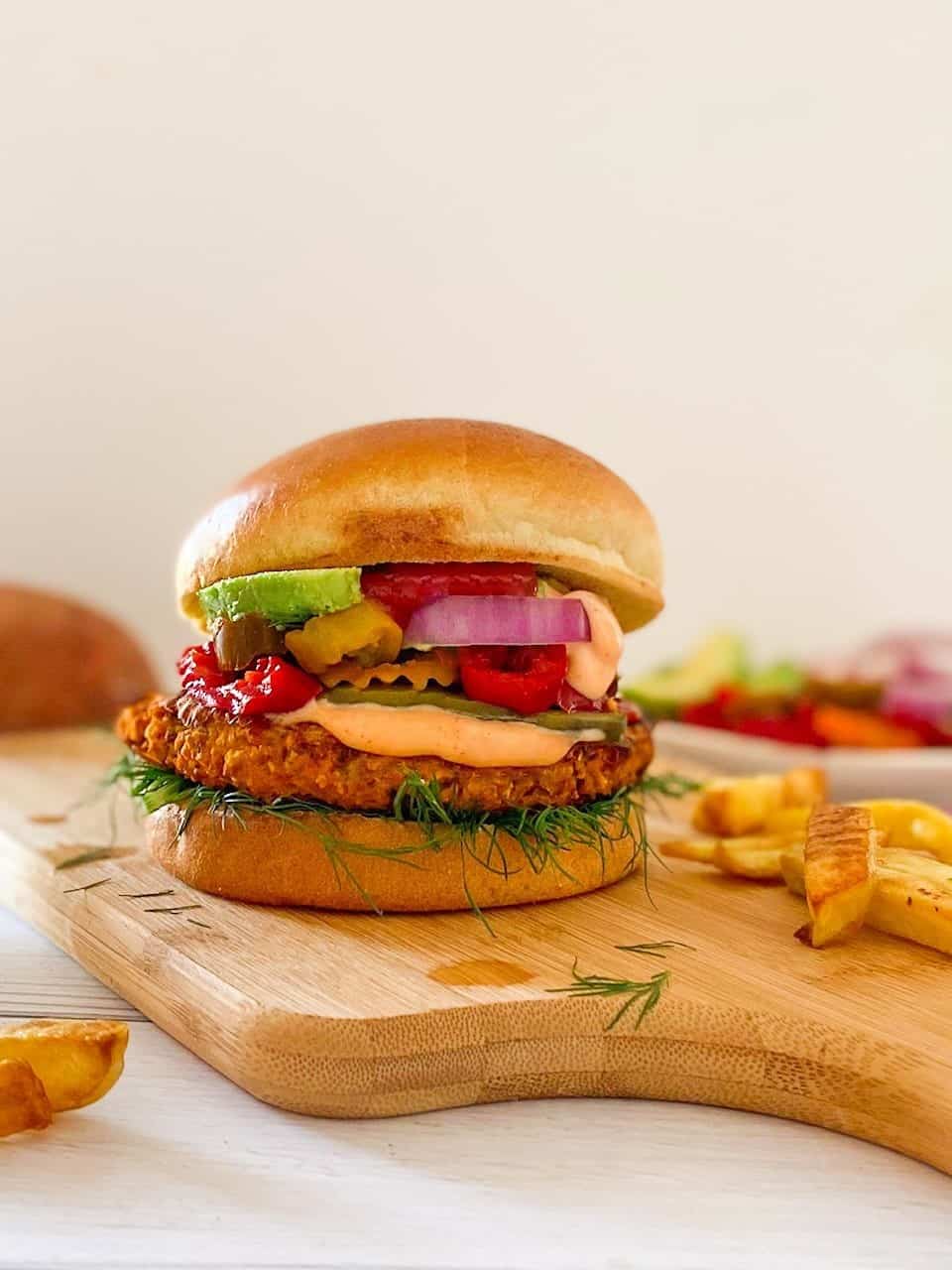 Veggie burger in bun with pickled jalapenos, avocado, onion and ketchup on cutting board.