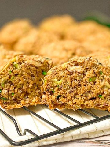 Zucchini muffin cut in half on cooling rack with more muffins behind.