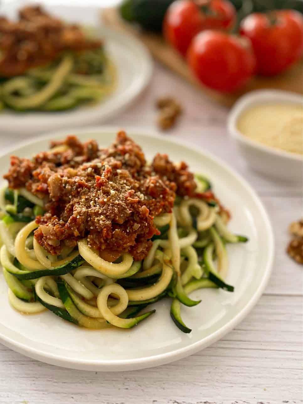 Plate of zoodles with bolognese sauce and vegan cheese on top.