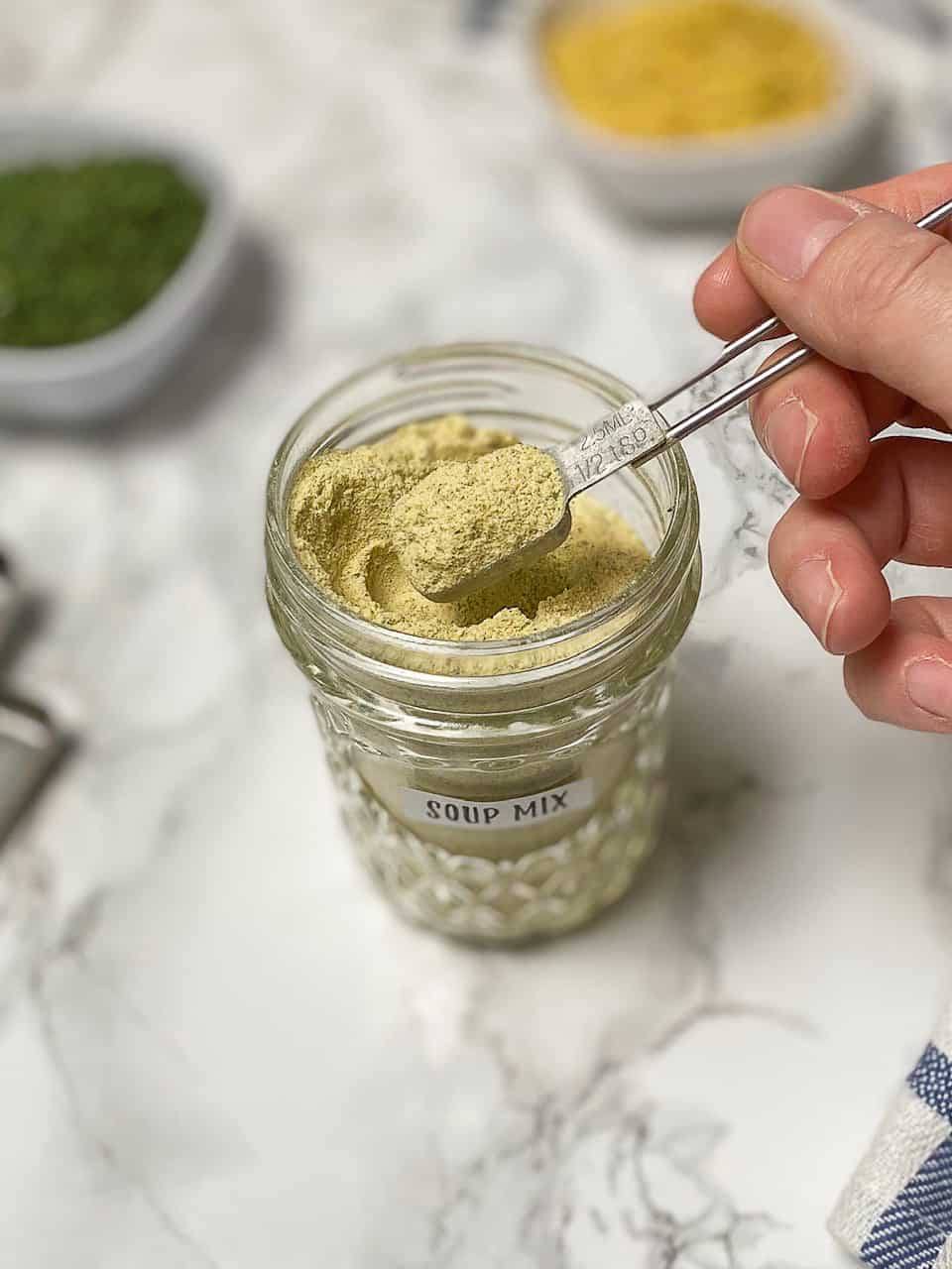 soup mix in glass jar with hand holding spoonful above