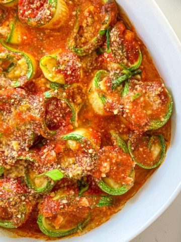 Zucchini lasagna roll ups in white baking dish.