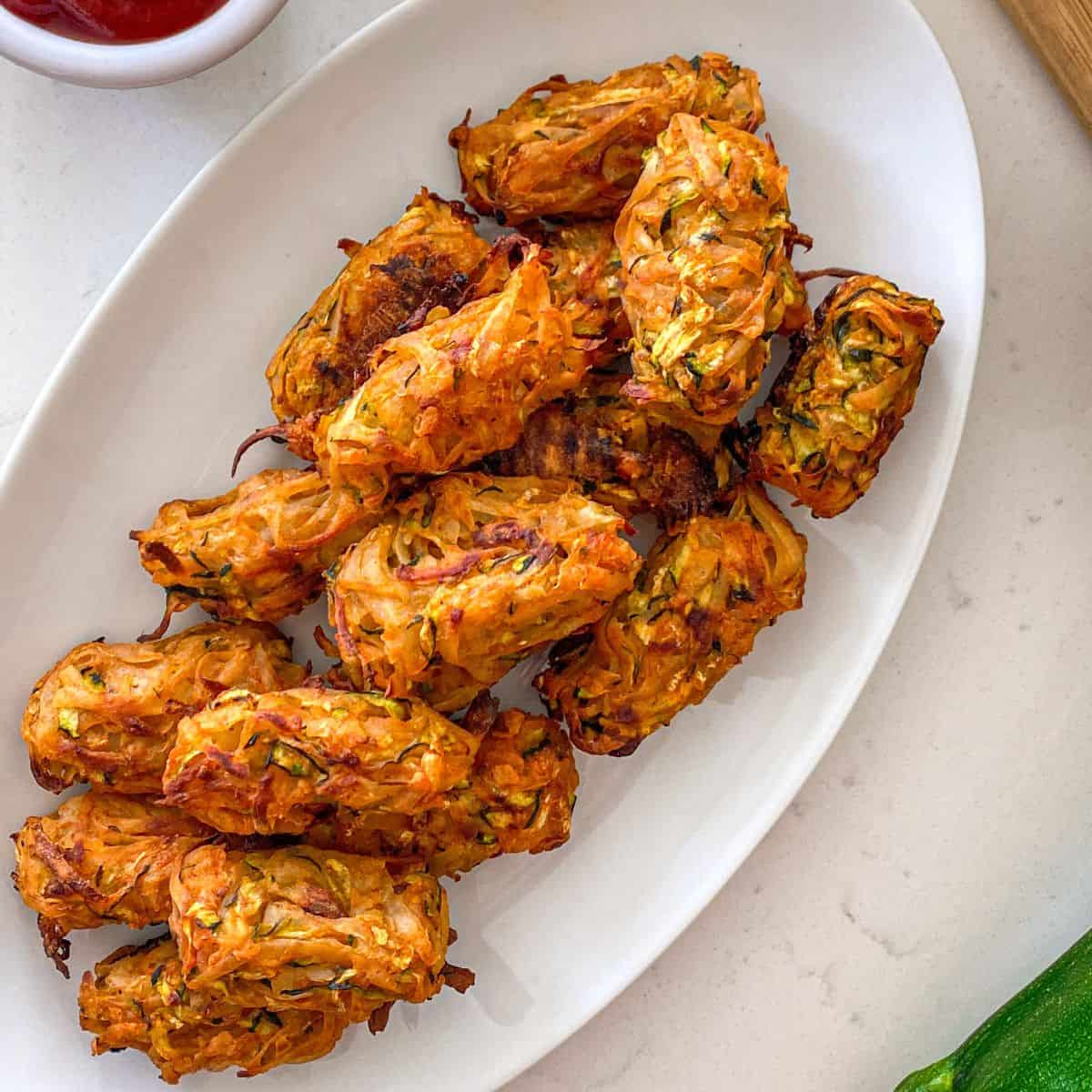 Baked zucchini tater tots in white, oval serving dish.